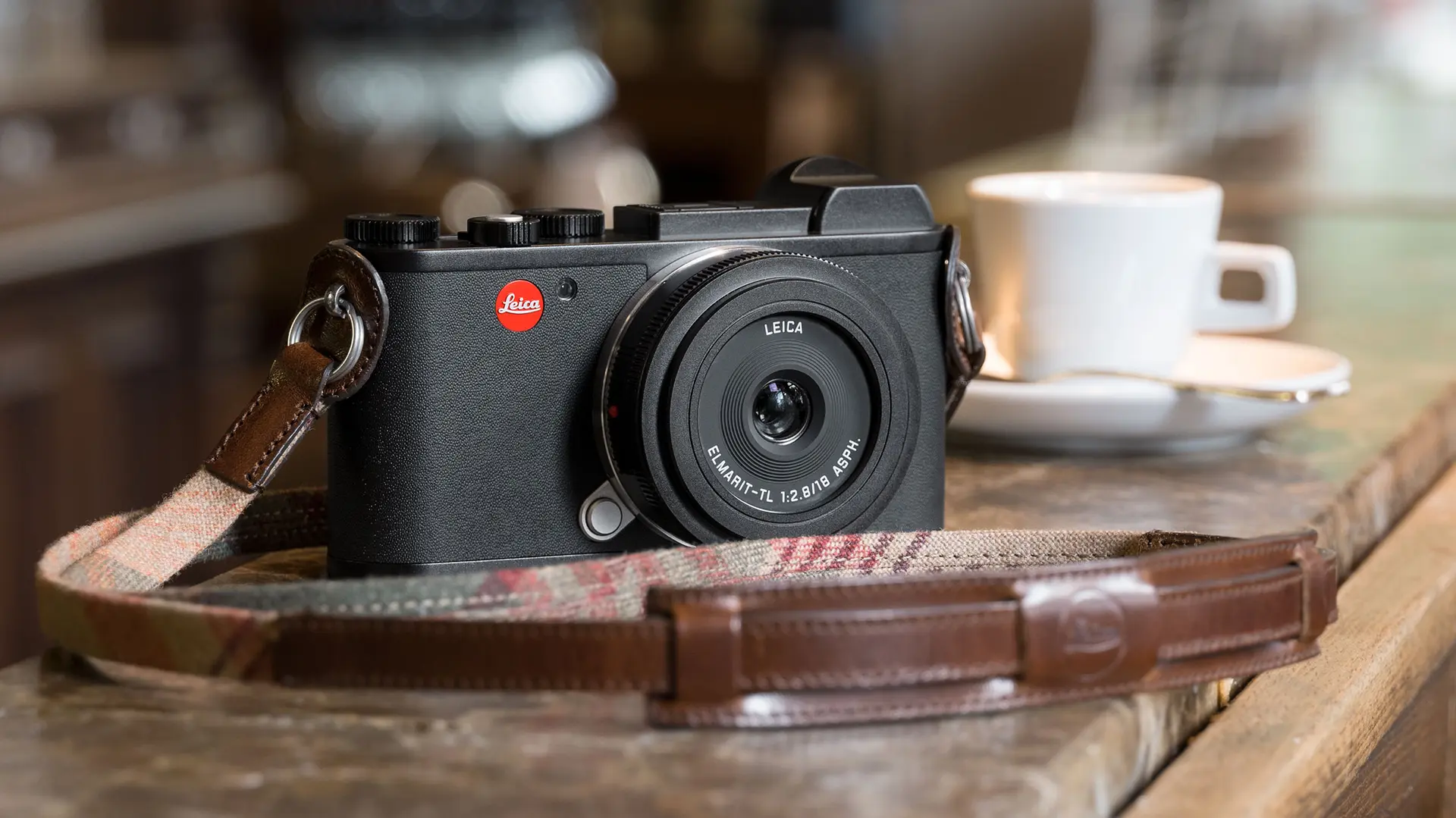 Leica camera on wooden counter with coffee cup in background