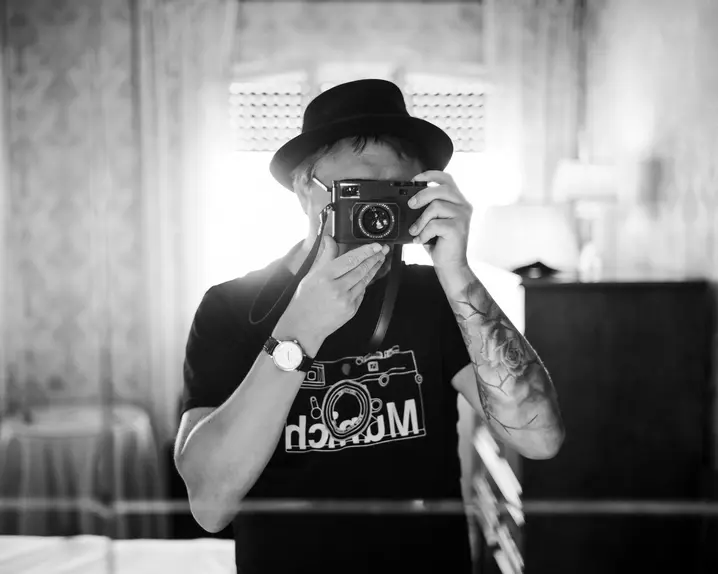 A person stands in a room and looks through a camera to take a photo.