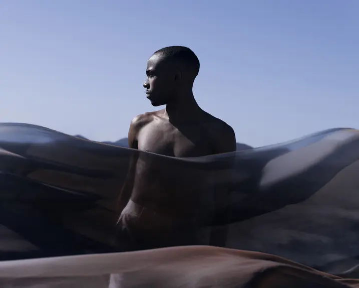 Man behind a transparent cloth looks to the side and light blue sky in the background.