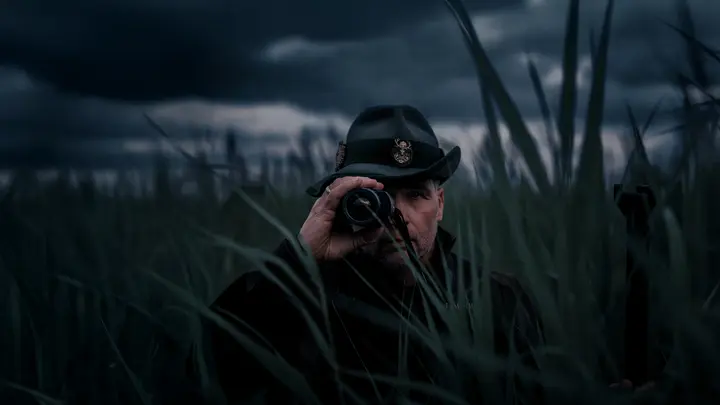 A hunter standing among tall grass at dusk with the Leica Calonox 2 in focus