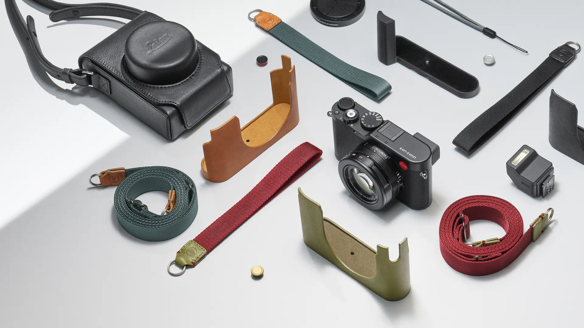 Leica camera with various straps, protective covers and accessories on a light background.