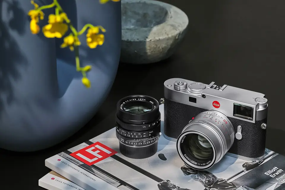 Leica M11 silver and Leica Summilux-M standing on LFI magazines on a table.