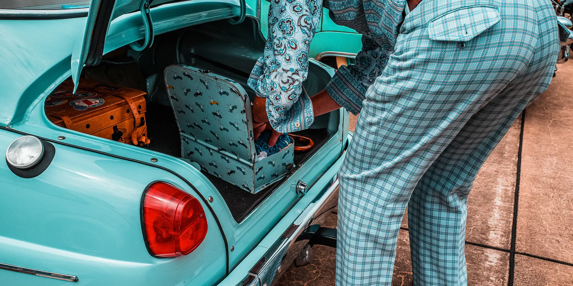A person packs suitcases into the trunk of a turquoise vintage car.