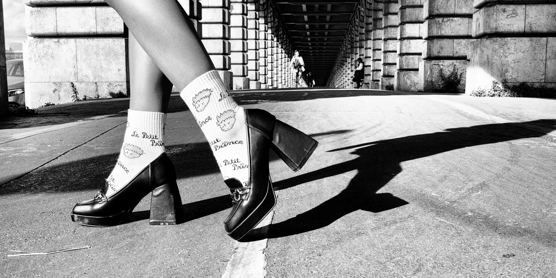 Close-up of legs in high heels on a street under a bridge in black and white.