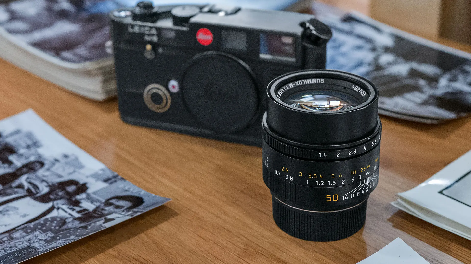 On the table are a camera, a camera lens and several stacks of black and white pictures.