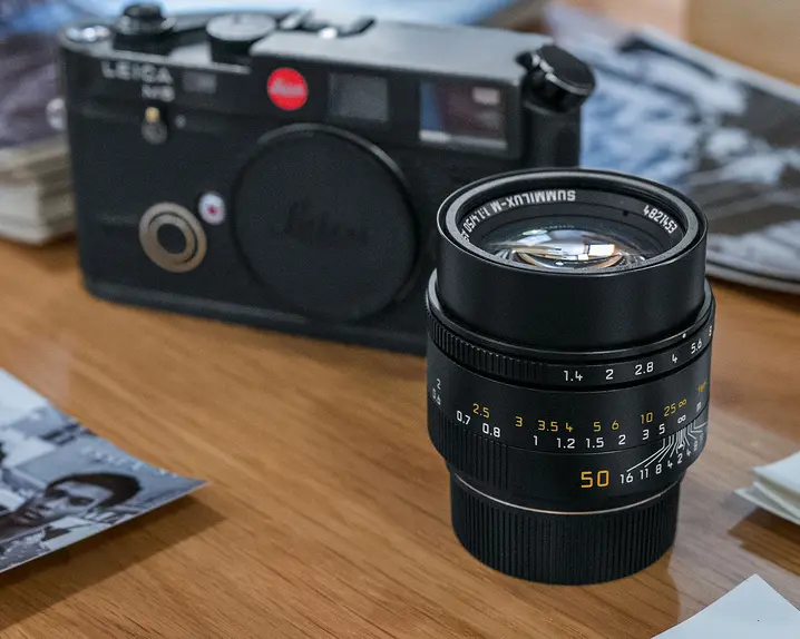 On the table are a camera, a camera lens and several stacks of black and white pictures.