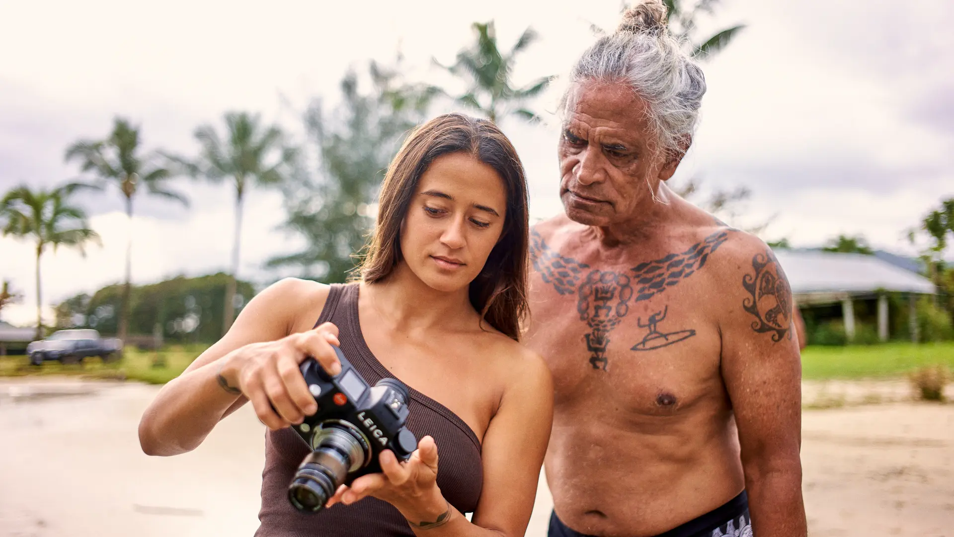 Mainei Kinimaka shows pictures on a camera to a man with Hawaiian tattoos on his upper body