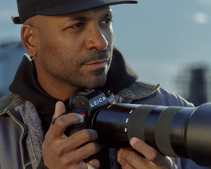 Close-up of a man holding a camera with skyscrapers in the background. 