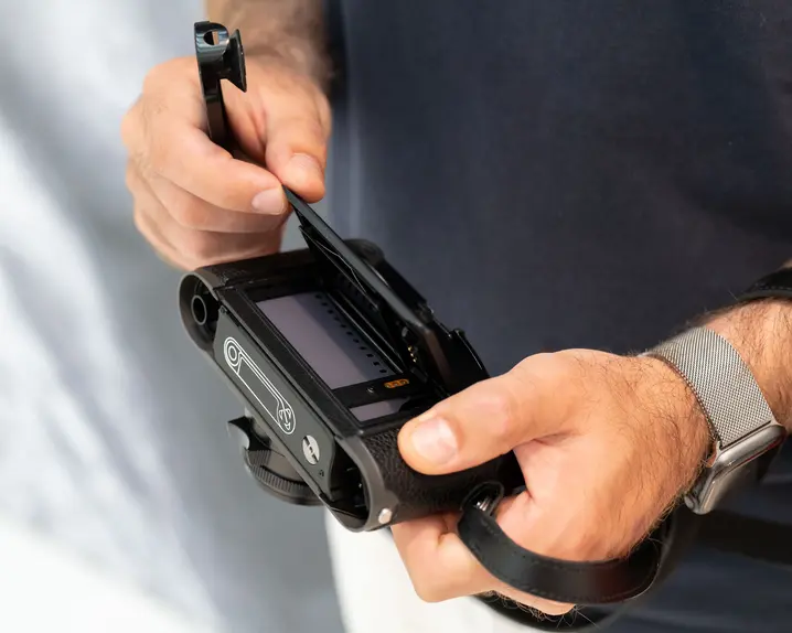 Close-up of the hands opening the back of the camera, where the camera roll is placed.
