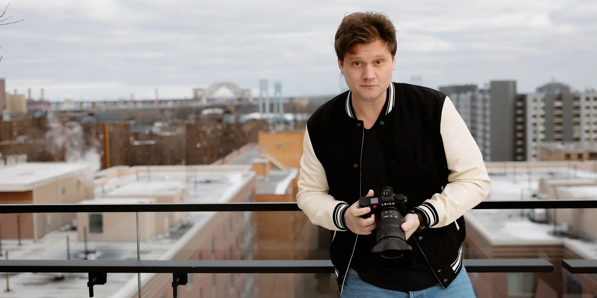 Person holding a camera, in the background are skyscrapers and a bridge on a cloudy day.