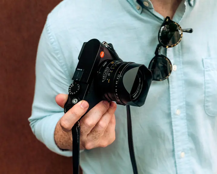 A man wearing a blue shirt holding a Leica camera in his right hand