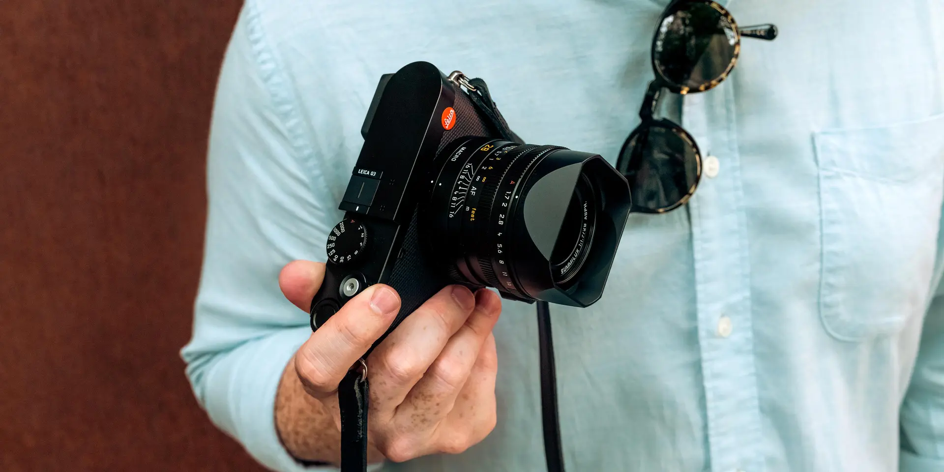 A man wearing a blue shirt holding a Leica camera in his right hand