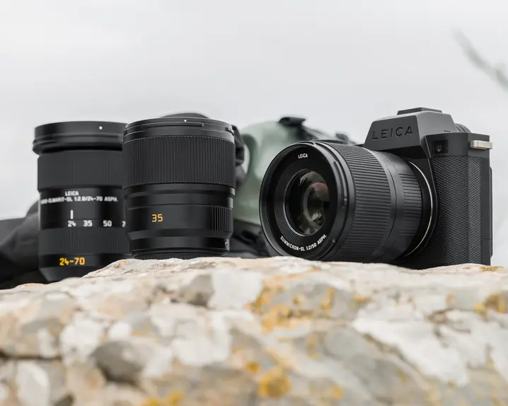 Leica cameras placed on a light-colored rock or stone with the sky in the background