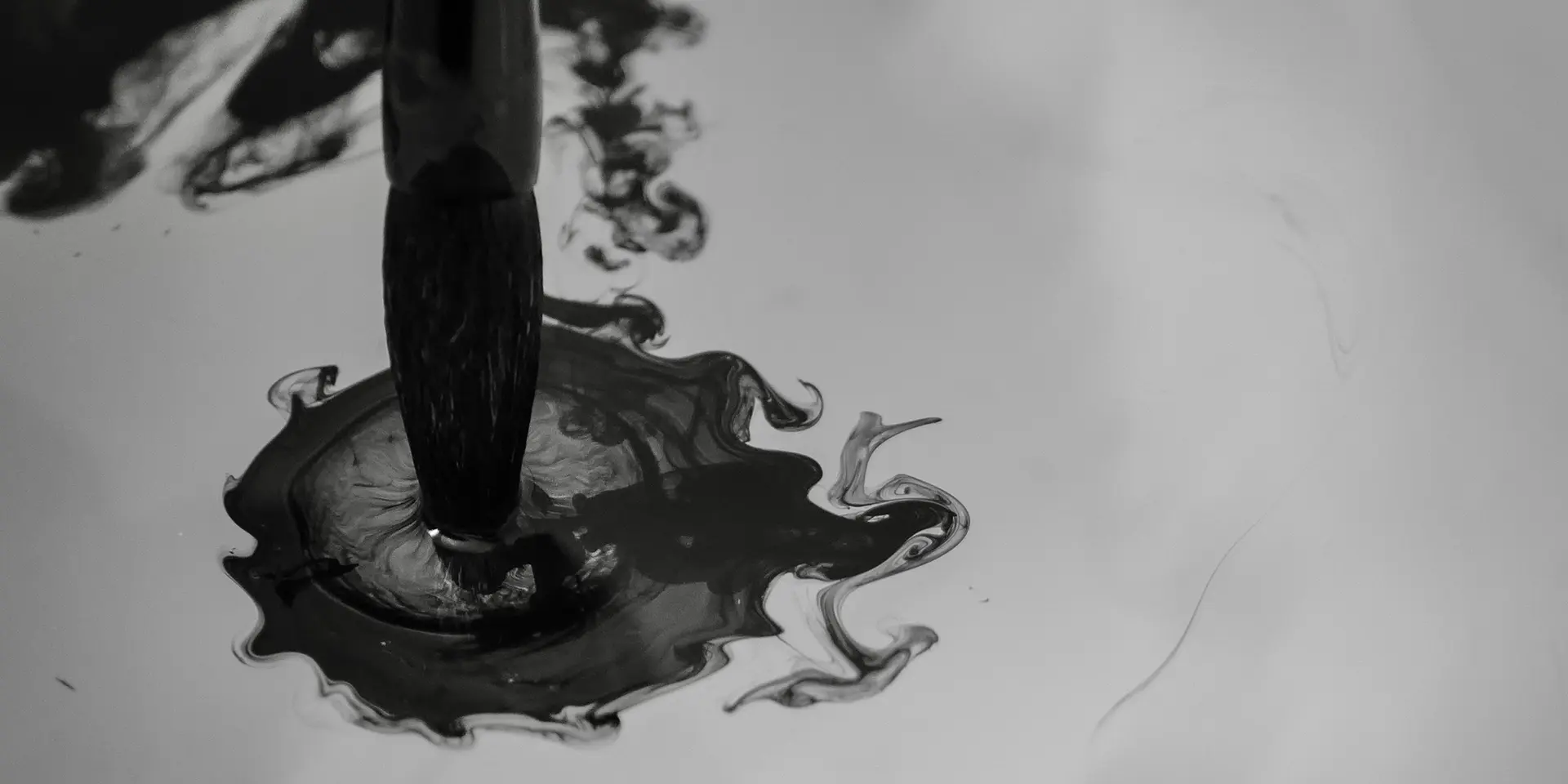 Brush dips into dark ink that spreads in the water.